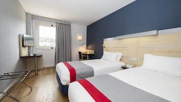 A hotel room with two beds, a desk, a chair, a TV, and a window with curtains.