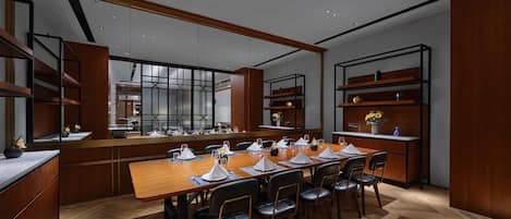 A modern dining area with a long wooden table set for a meal, surrounded by black chairs.