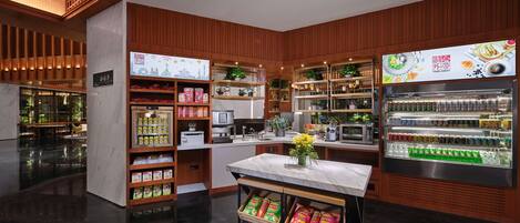 A modern interior with wooden paneling, a central island with a vase, and shelves stocked with snacks and beverages.