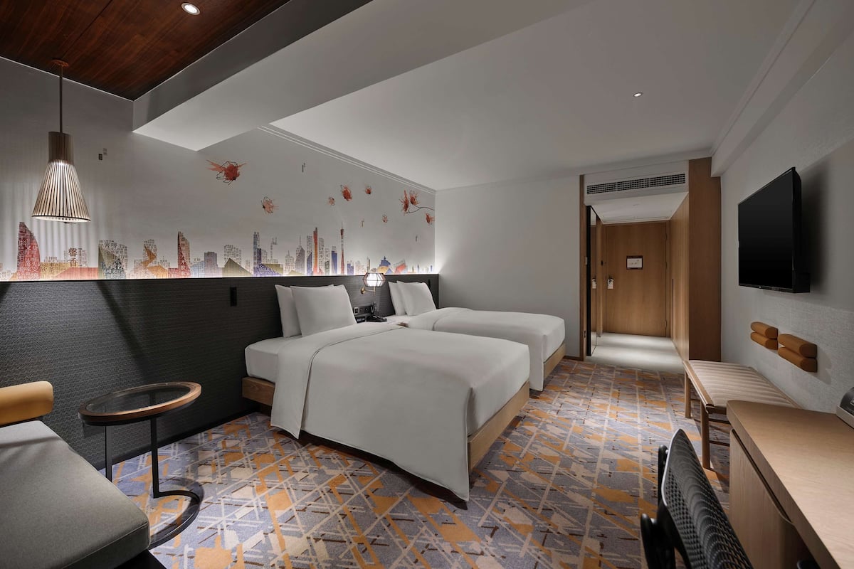 A modern hotel room with a bed, bedside tables, a seating area, and a TV.