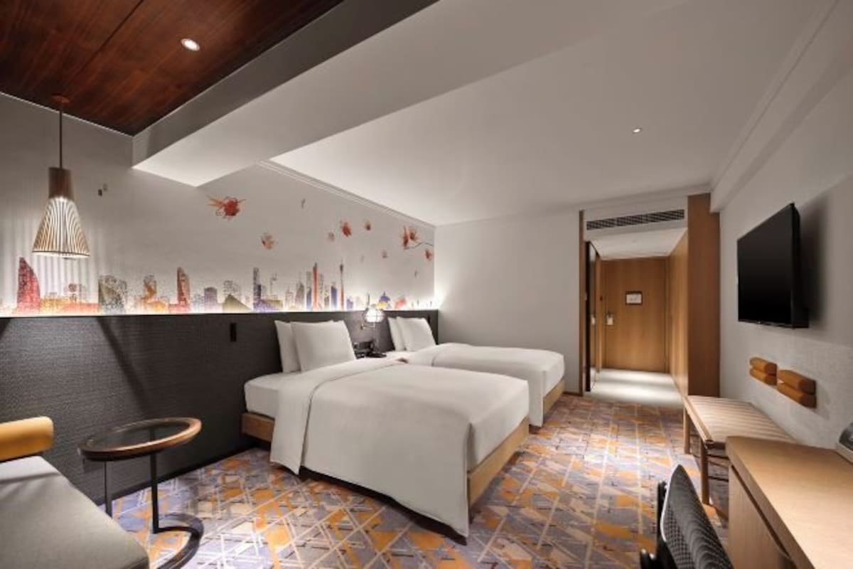 A hotel room with two beds, a small table, a chair, a TV, and a patterned floor.