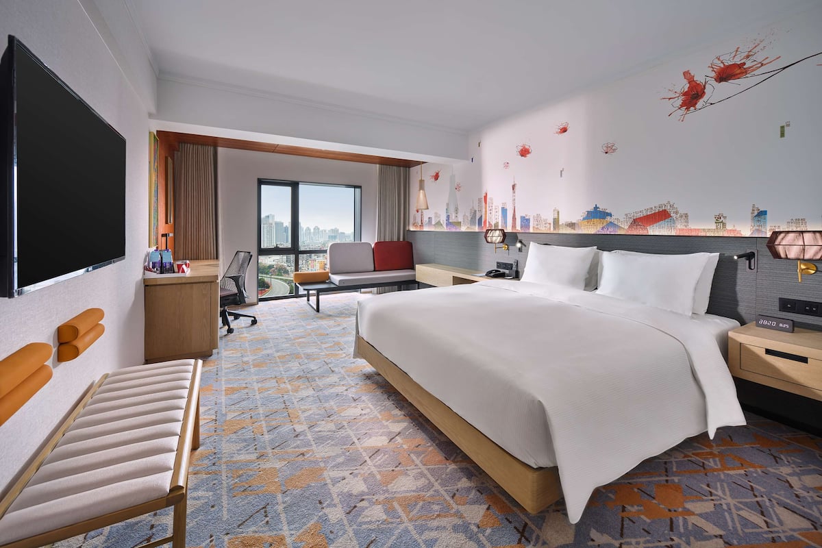 A hotel room with a large bed, a desk, a chair, and a TV.