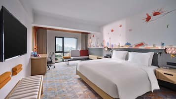 Quarto de hotel com uma cama grande, uma escrivaninha, uma cadeira e uma televisão.