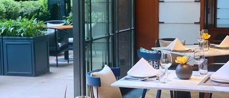 Een buiten eethoek met tafels voor twee personen, voorzien van witte borden, bestek en glazen.