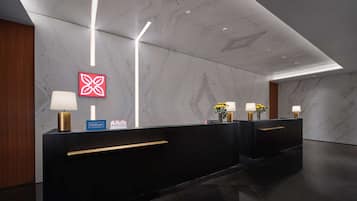 A modern hotel reception area with marble walls, a reception desk, and two lamps with yellow flowers.