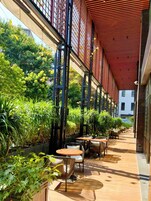 Un patio al aire libre con mesas y sillas, rodeado de exuberante vegetación y un techo rojo.