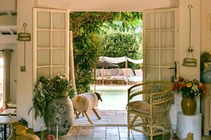An open doorway leading to a pool area with a wicker chair and a vase of flowers. - La Bastide D'Antoine (Gassin)