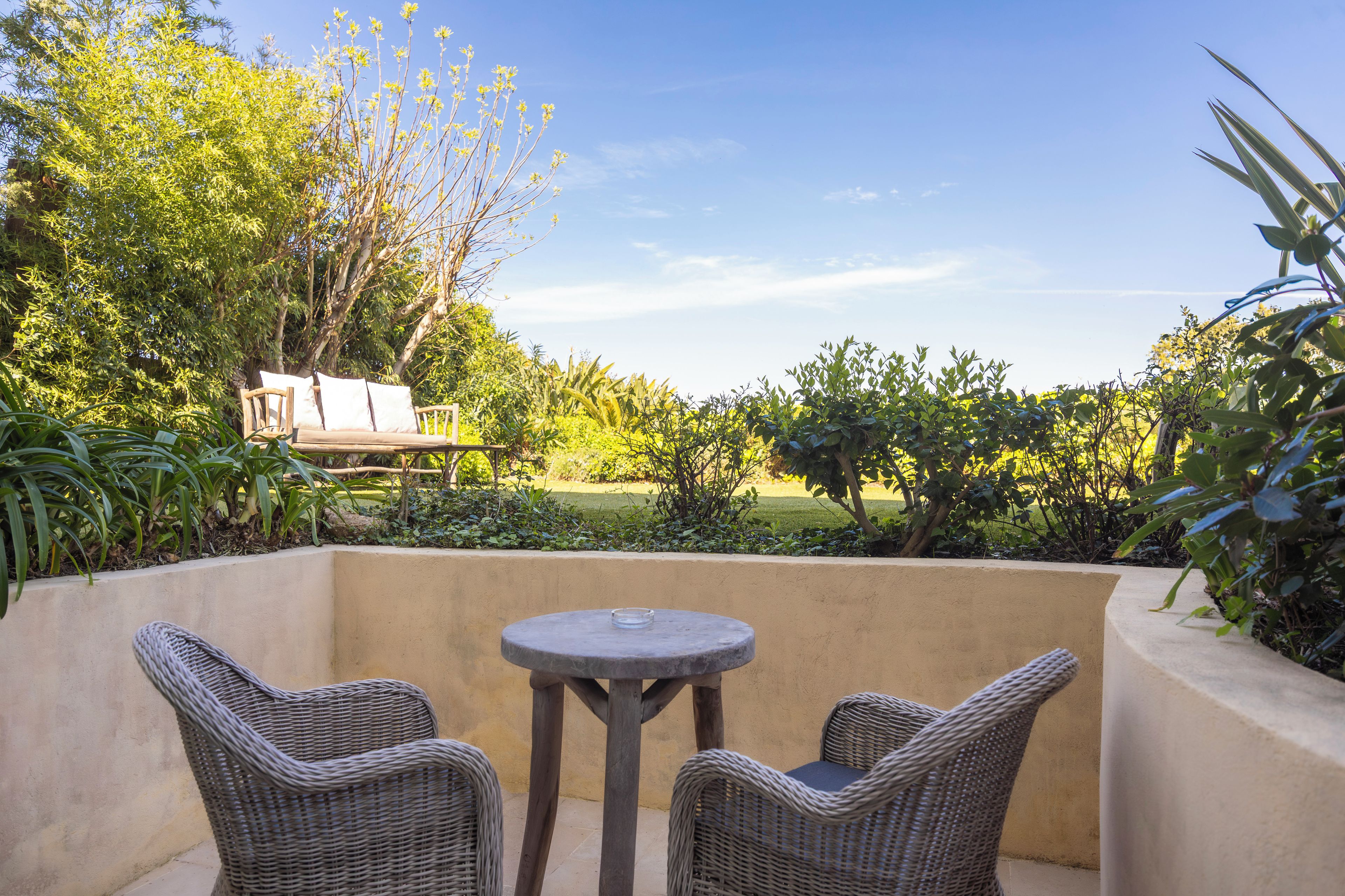 A patio with wicker furniture, a round table, and a view of a garden and lawn.