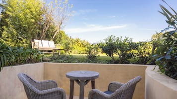 A patio with wicker furniture, a round table, and a view of a garden and lawn.