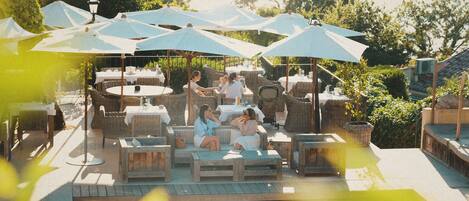 An outdoor pool area with lounge chairs and umbrellas, surrounded by greenery.