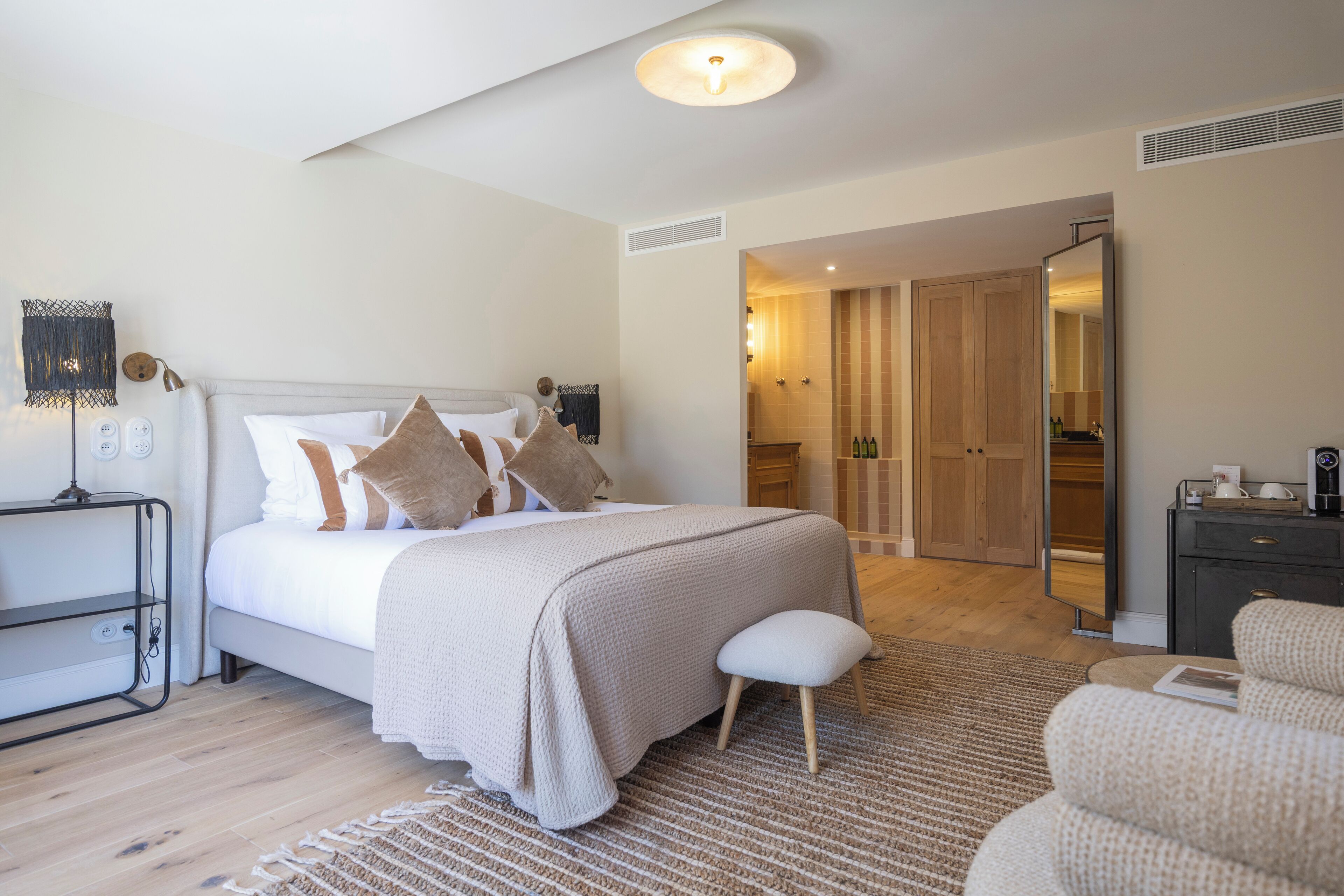Une chambre à coucher moderne avec un grand lit, des tables de chevet, un petit tabouret et un dressing.