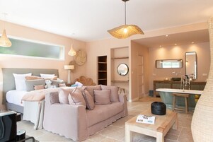 Una habitación de hotel moderna con cama, sofá, mesa de comedor y baño con bañera y lavamanos.