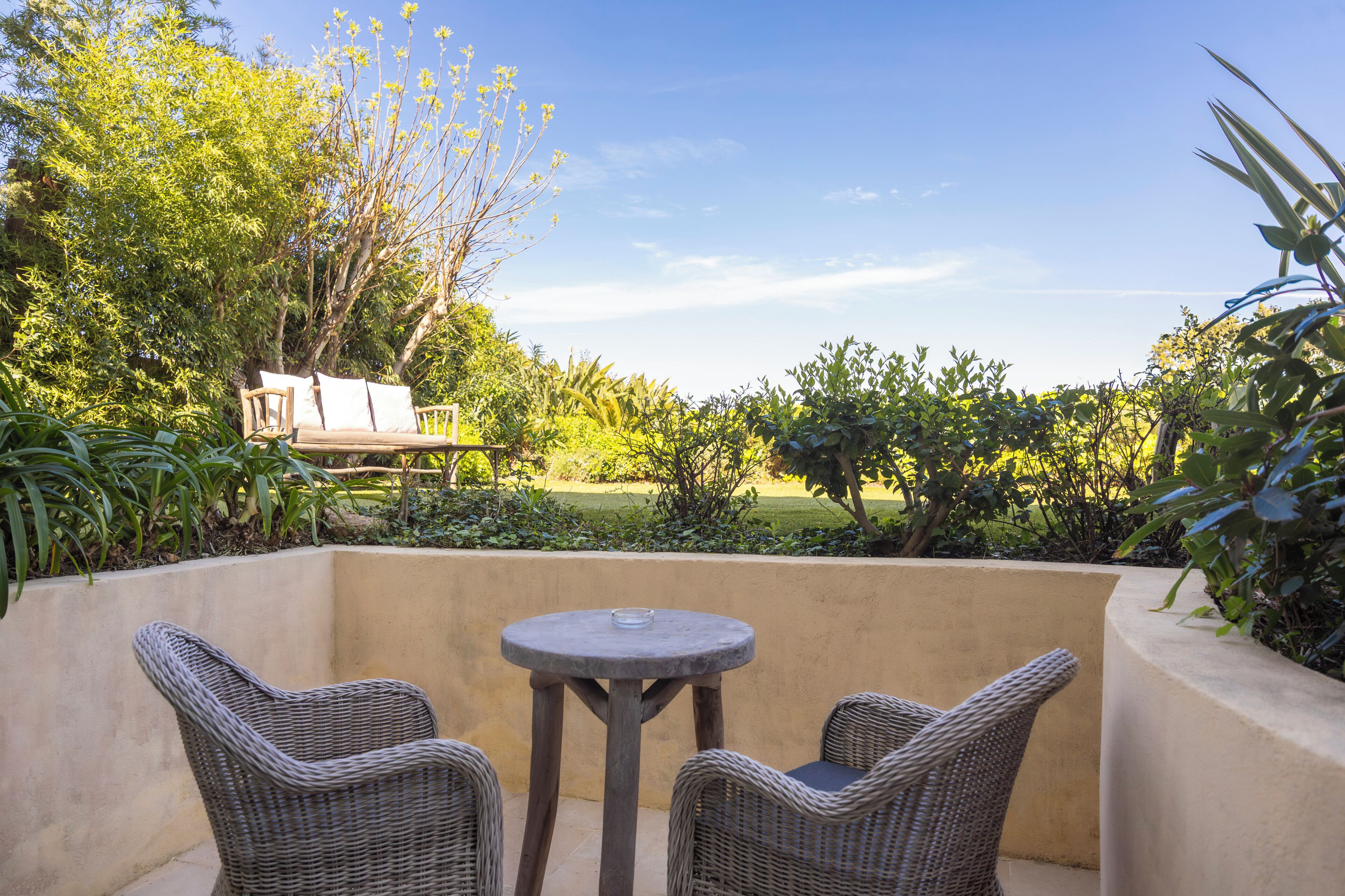 Un patio con mobiliario de mimbre, una mesa redonda y vistas a un jardín y césped.