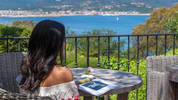A person seated at a round table with a view of a coastal landscape.