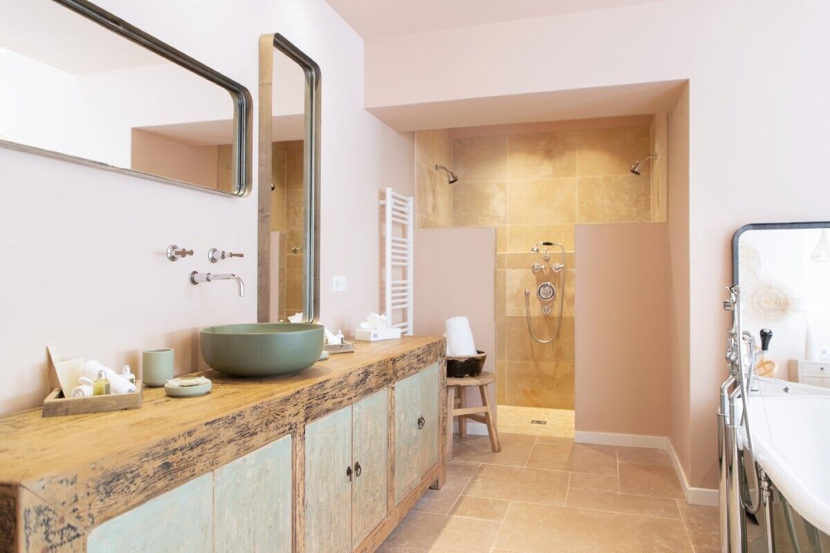 A bathroom with a large mirror, a wooden vanity, a large bowl sink, a shower area, and a bathtub.