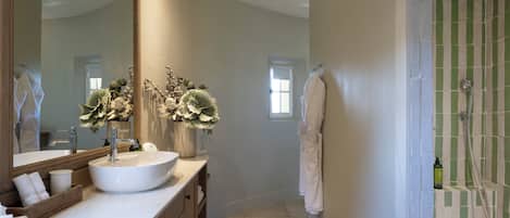 Un baño con un espejo grande, un lavamanos blanco, un armario de madera y una zona de ducha con azulejos verdes.