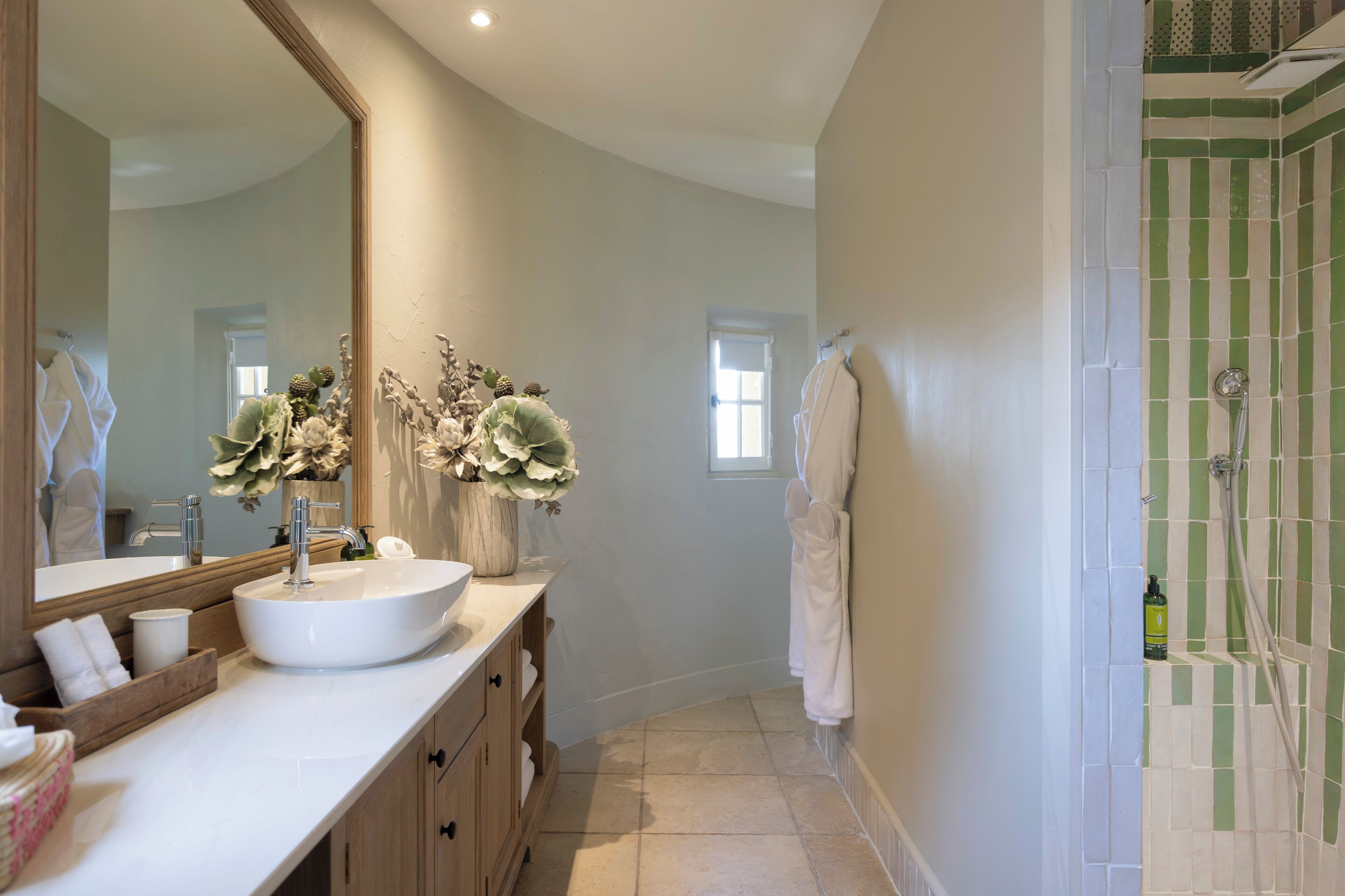 A bathroom with a large mirror, a white sink, a wooden vanity, a shower with green tiles, and a towel rack.