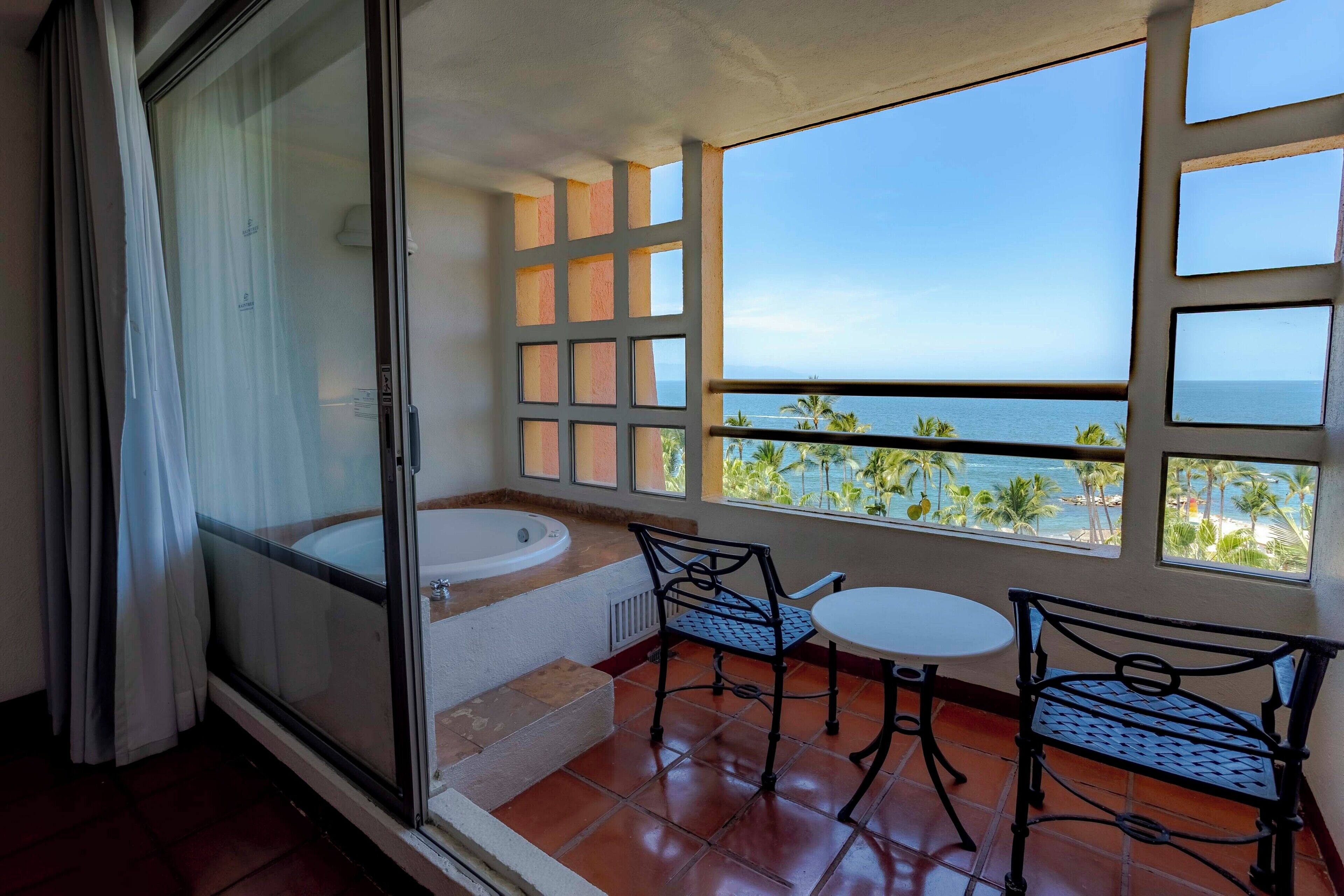 A balcony with a view of the sea, a bathtub, and two chairs.