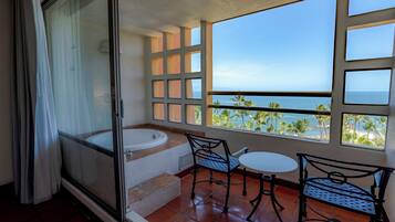 A balcony with a view of the sea, a bathtub, and two chairs.