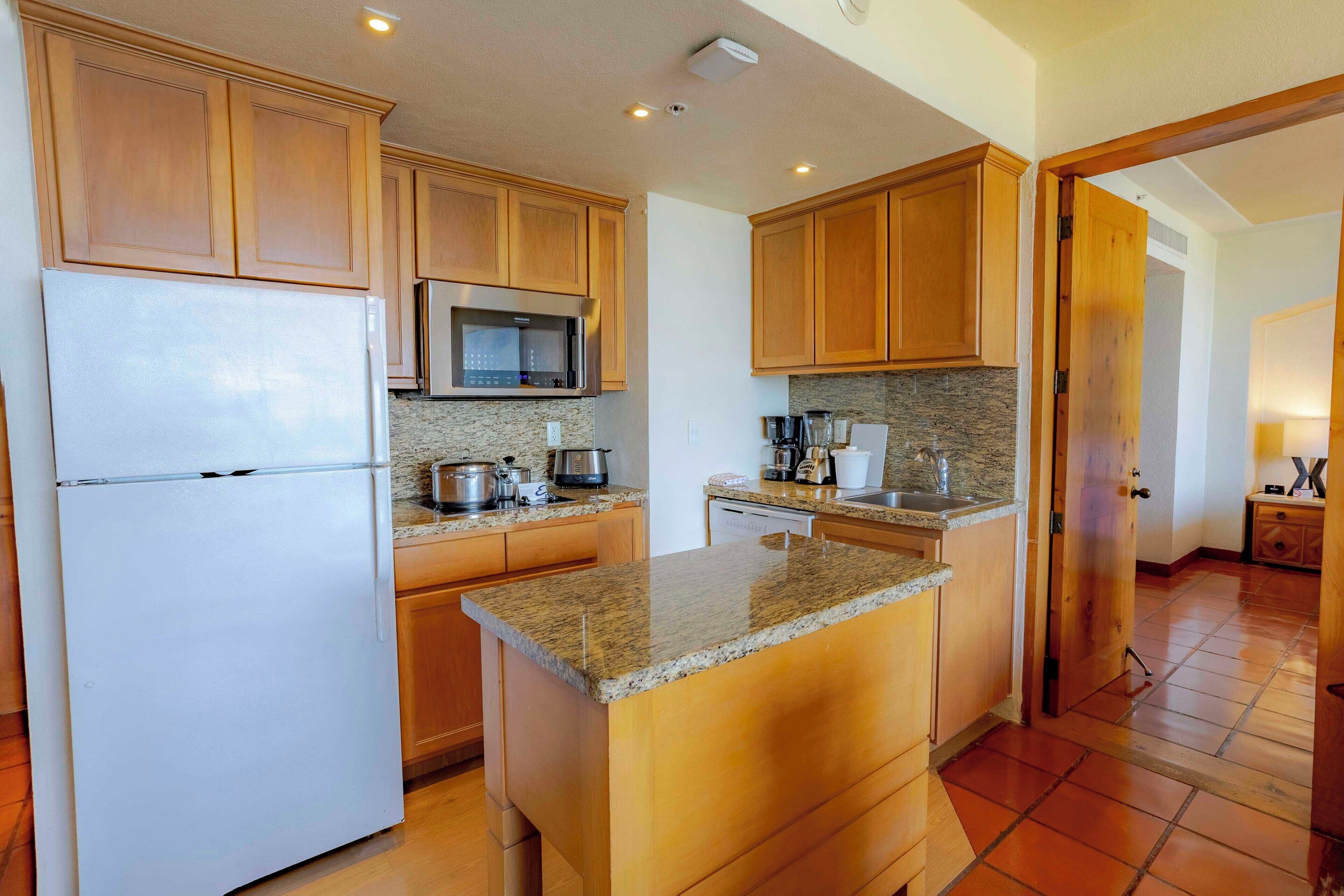 A kitchen with wooden cabinets, a stainless steel refrigerator, a microwave, and a granite countertop island.