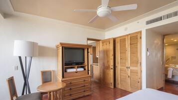 A hotel room with a bed, a TV, wooden furniture, a ceiling fan, and a bathroom visible through an open door.