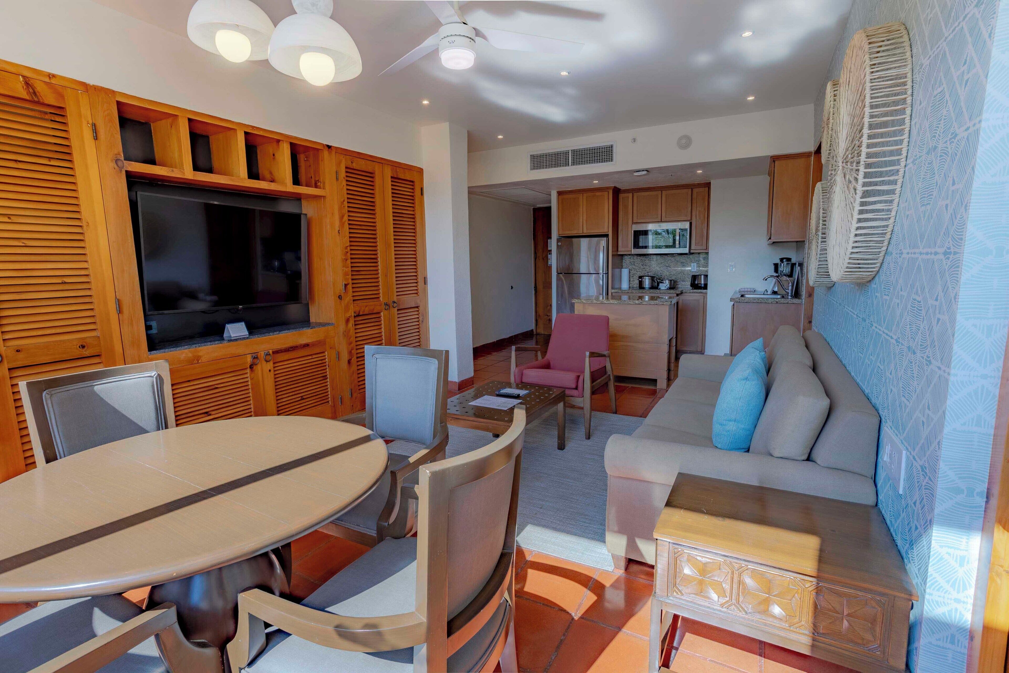 A modern living room with a dining area, a kitchen, and a TV mounted on a wooden wall.