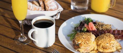 A breakfast setting with croissants, a plate of eggs, a glass of orange juice, a cup of coffee, and a pitcher of water on a wooden table.