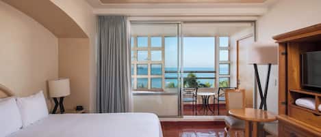 Habitación de hotel con cama, televisión, balcón con mesa y sillas, y vista al océano.