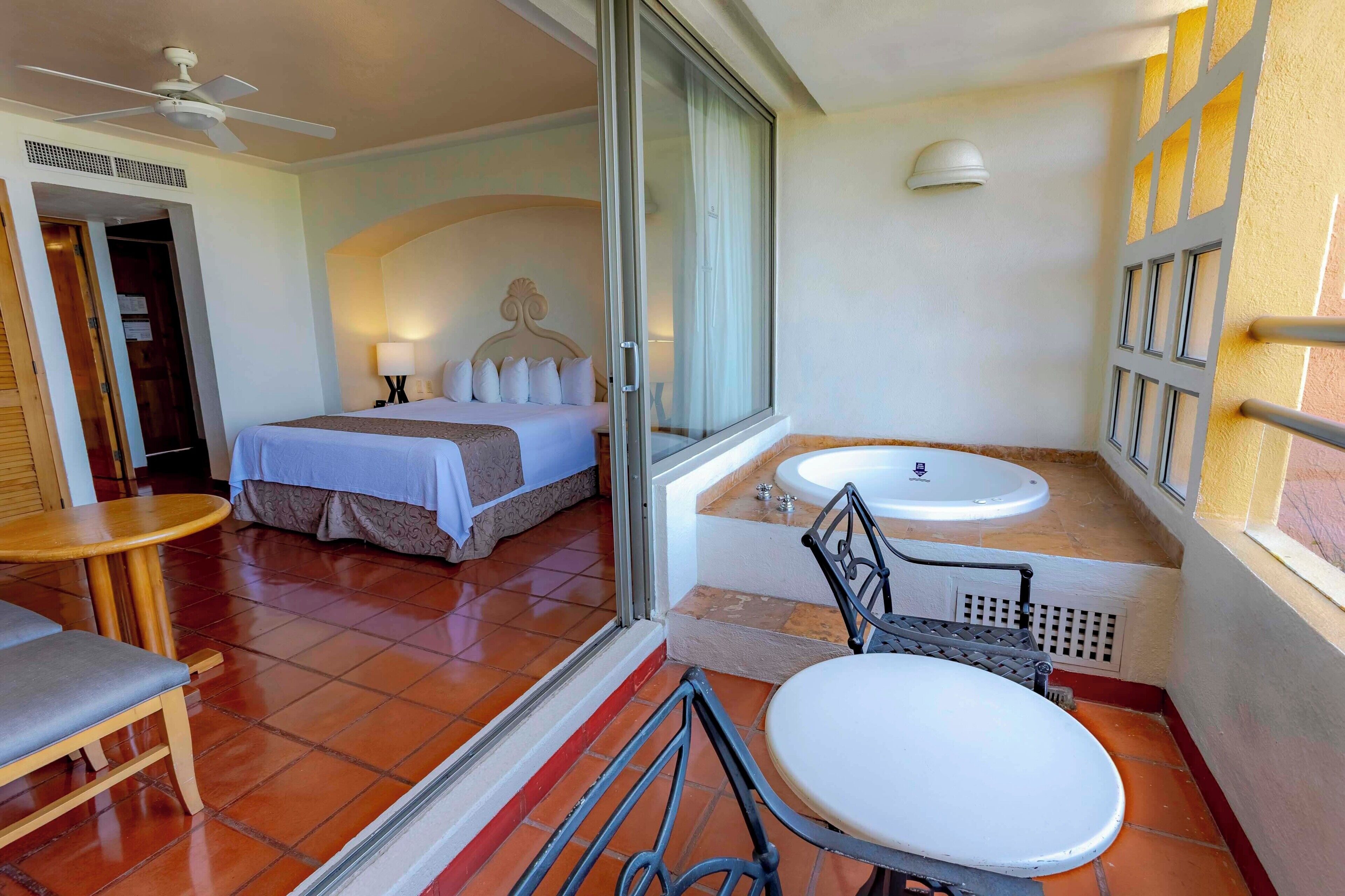 A hotel room with a bed, a bathroom with a bathtub, a small table, and a chair.
