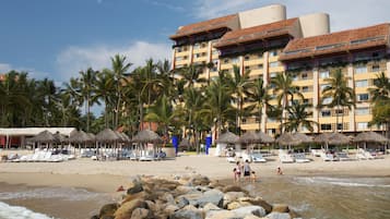 A beachfront hotel with multiple balconies, palm trees, and beach umbrellas.