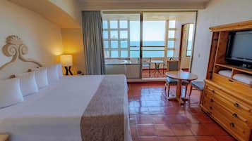 Habitación de hotel con cama, televisión, balcón con mesa y sillas, y vista al mar.