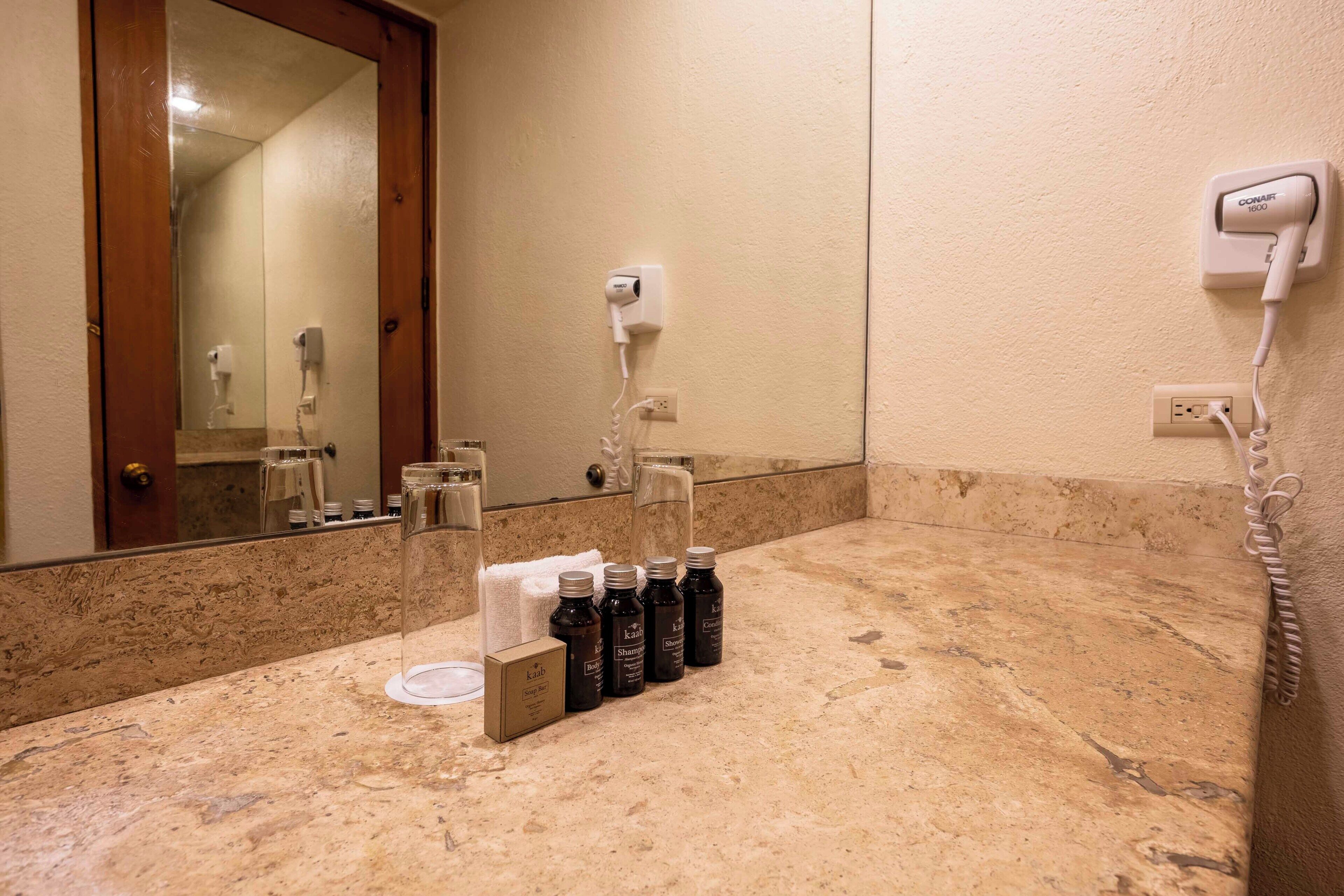Een badkamer met een marmeren aanrecht, een haardroger, een zeepstaaf en diverse flessen shampoo en conditioner.