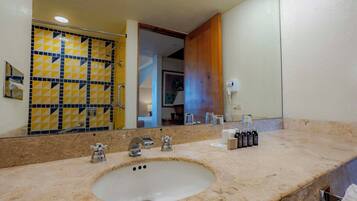 A bathroom with a sink, three faucets, a mirror, and a shower area with yellow and blue tiles.