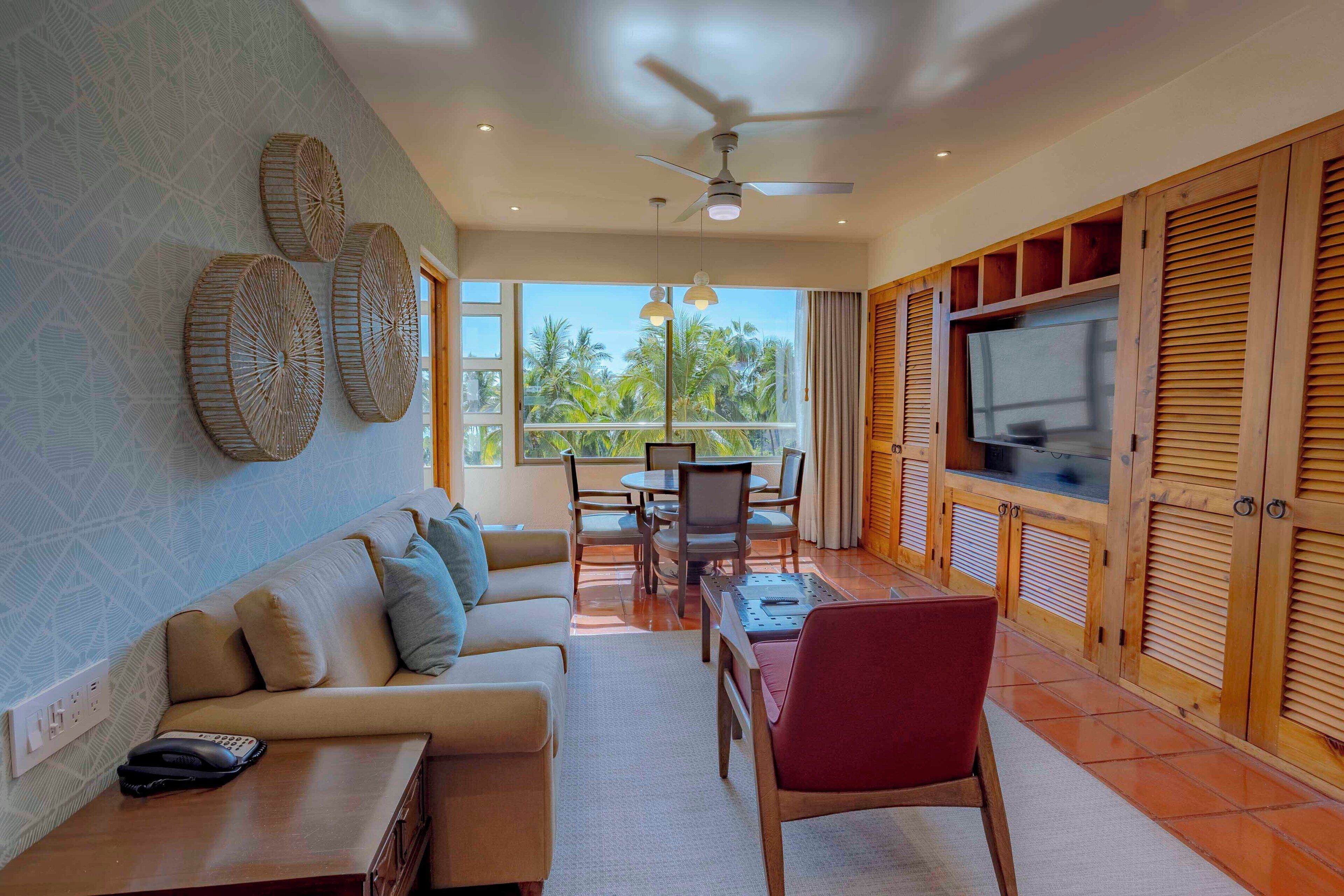 A living room with a sofa, chairs, a TV, and a balcony with a view.