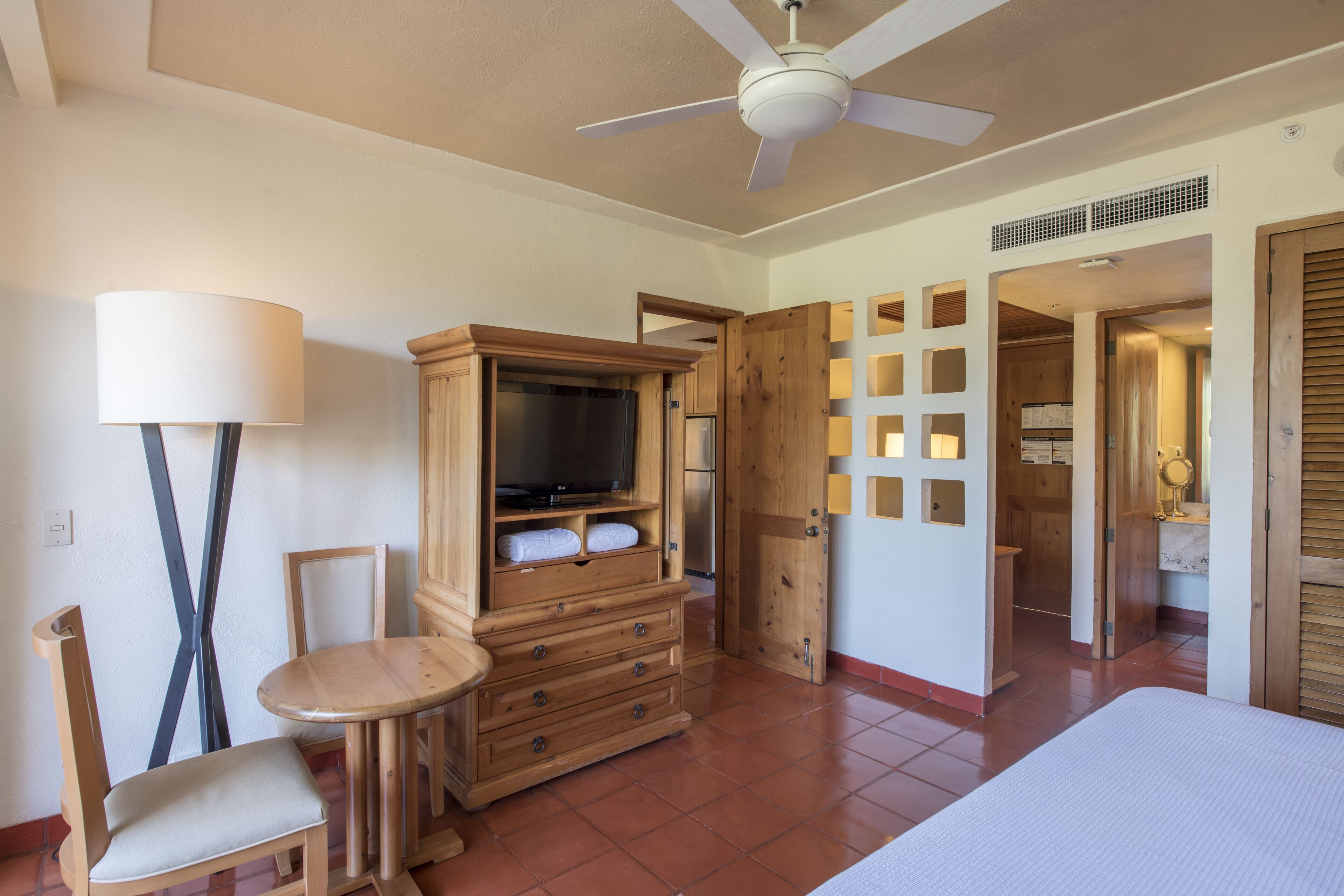 Ein Hotelzimmer mit Holzschrank, Fernseher, Stuhl, Tisch und Deckenventilator.
