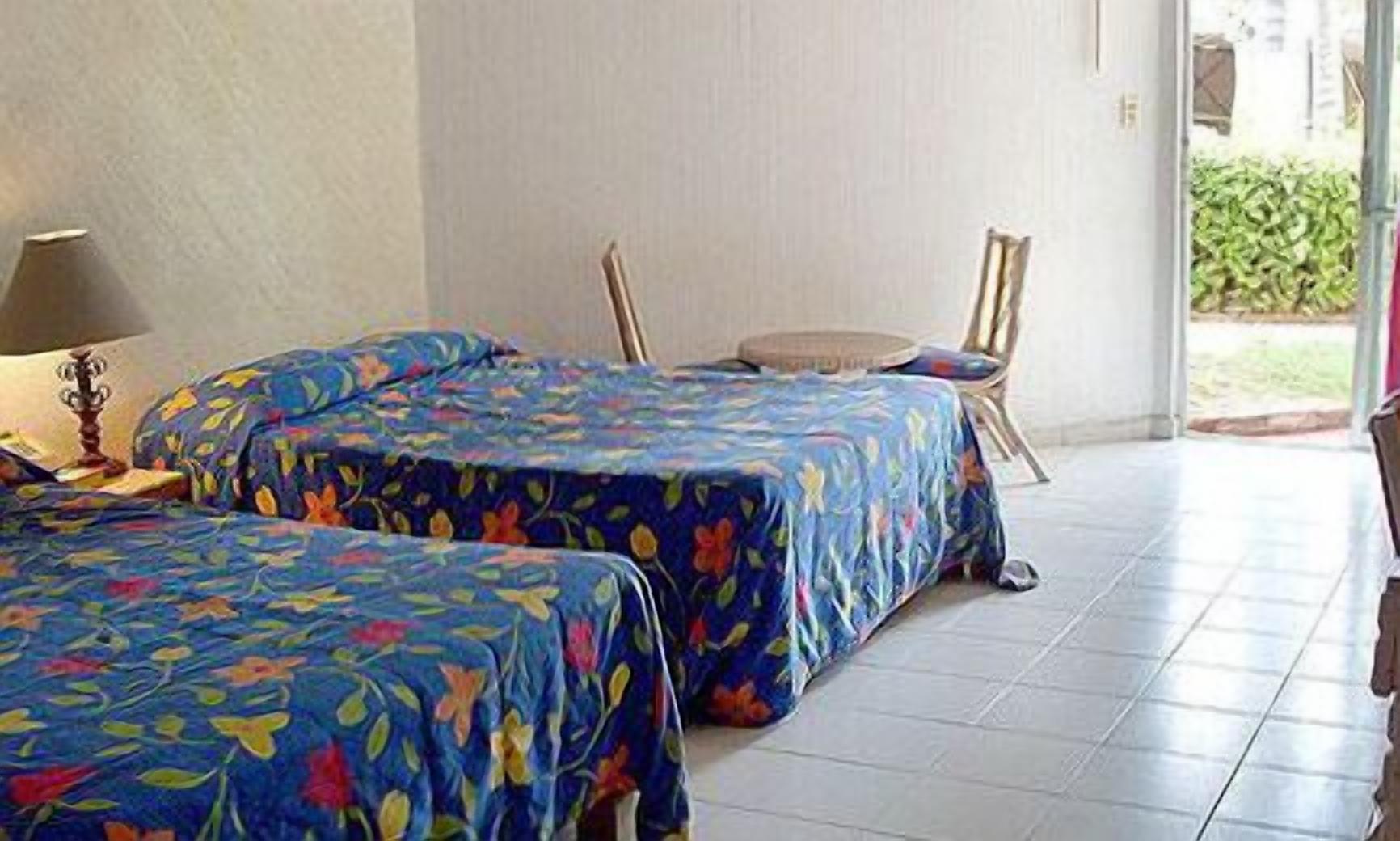 Une chambre d’hôtel avec deux lits recouverts de couvre-lits à motifs floraux, une petite table et une chaise.