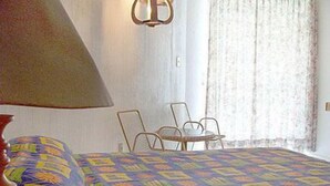 A hotel room with a bed, a table, two chairs, a lamp, and a window with curtains. - El Tropicano (Acapulco)