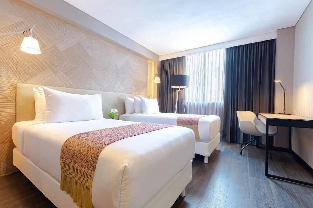 Een hotelkamer met twee bedden, een bureau, een stoel en een groot raam met gordijnen.