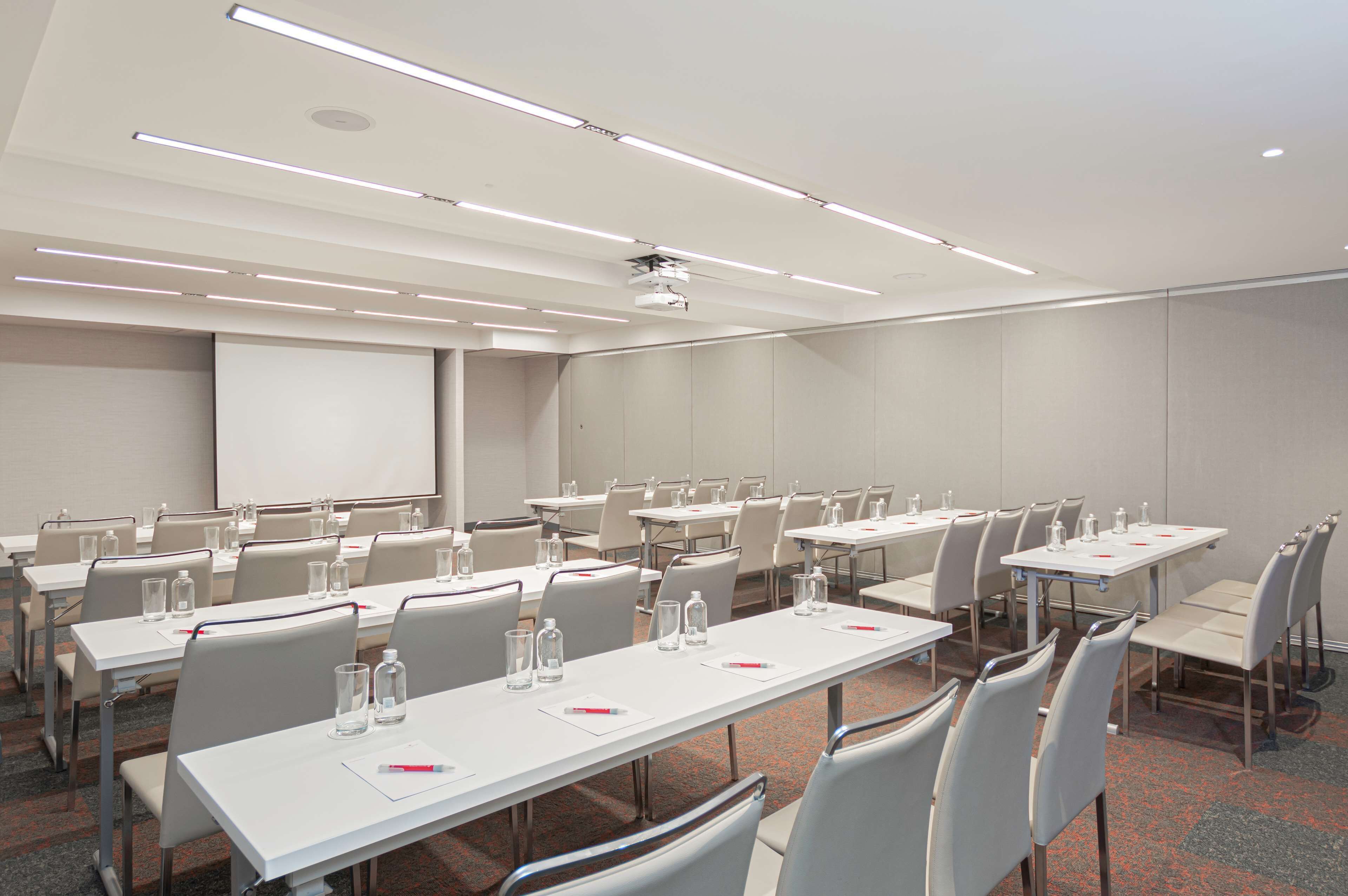 A conference room with white tables, chairs, and a projector screen.