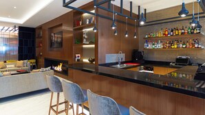 Zona de bar moderna con mostrador de madera, taburetes y una variedad de botellas de licor.