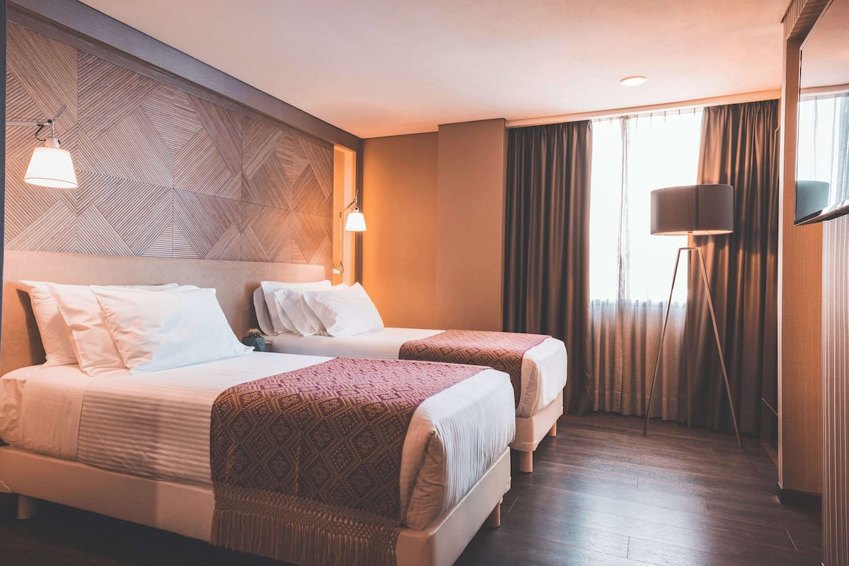 Een hotelkamer met twee bedden, een grote spiegel, een vloerlamp en een kamer met een patroon op de muur.