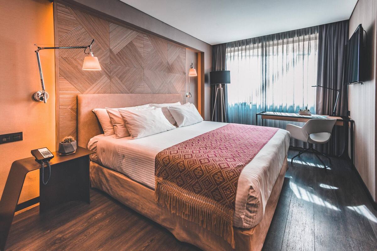 Een moderne hotelkamer met een groot bed, een bureau, een stoel, een bureaulamp, een telefoon en een aan de muur bevestigde televisie.