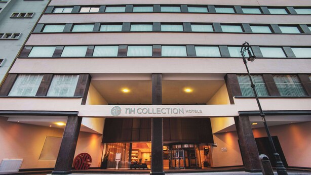 Entrada de un hotel con fachada moderna, grandes ventanales y un cartel llamativo que dice "NH Collection Hotels".