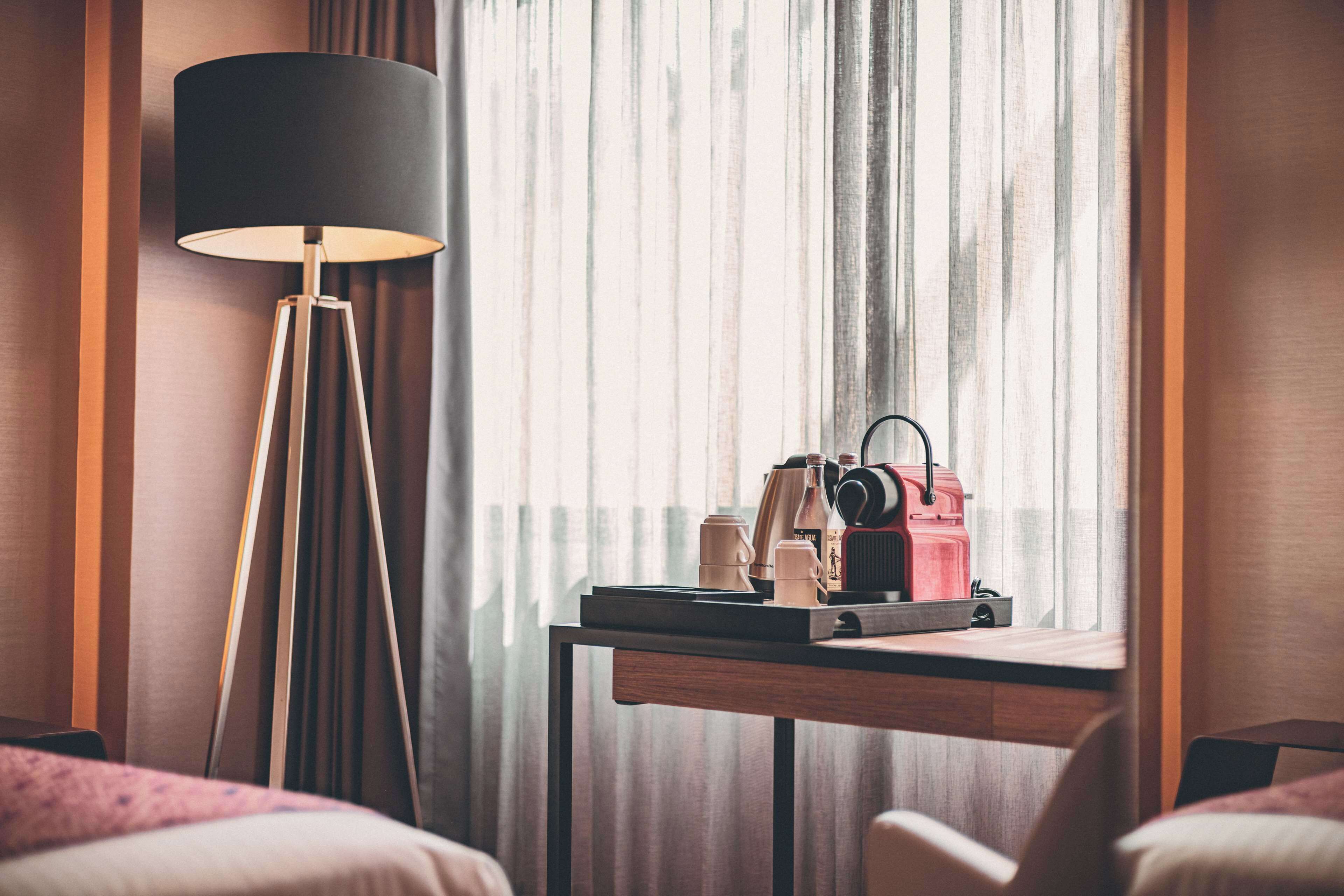 Une chambre d’hôtel avec un bureau, une lampe et une fenêtre avec des rideaux.