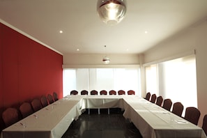 Un salón de conferencias con una larga mesa, paredes acolchadas rojas y ventanas amplias.