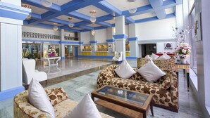 A spacious lobby with a high ceiling, blue accents, a central seating area with patterned sofas, and a reception desk. - Palms Hotel (Mumbai)