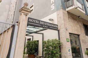 The entrance to HOTEL DES ETRANGERS with a sign above the door, a glass door, and potted plants in front. - Hotel Des Etrangers (Milan)