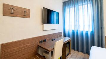 Une chambre d’hôtel moderne avec un bureau en bois, un téléviseur à écran plat, un lit et une fenêtre avec des rideaux bleus.