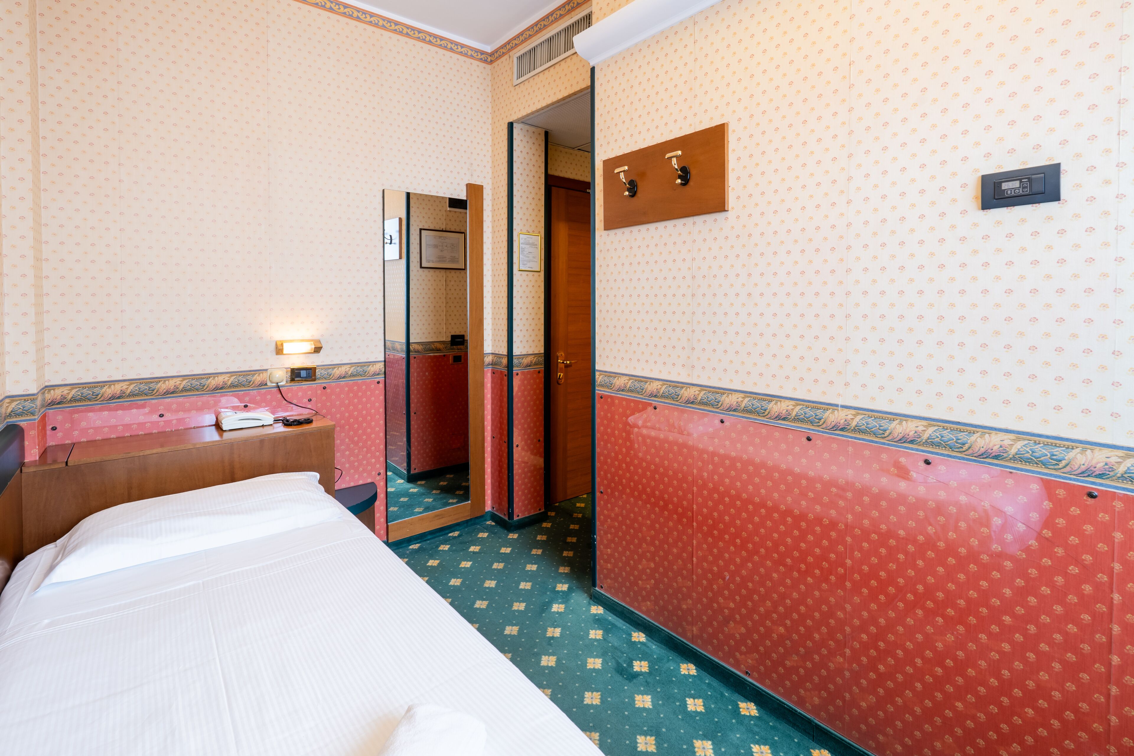 Une chambre d’hôtel avec un lit, un petit bureau doté d’une lampe, un miroir et une coiffeuse rouge avec un lavabo.