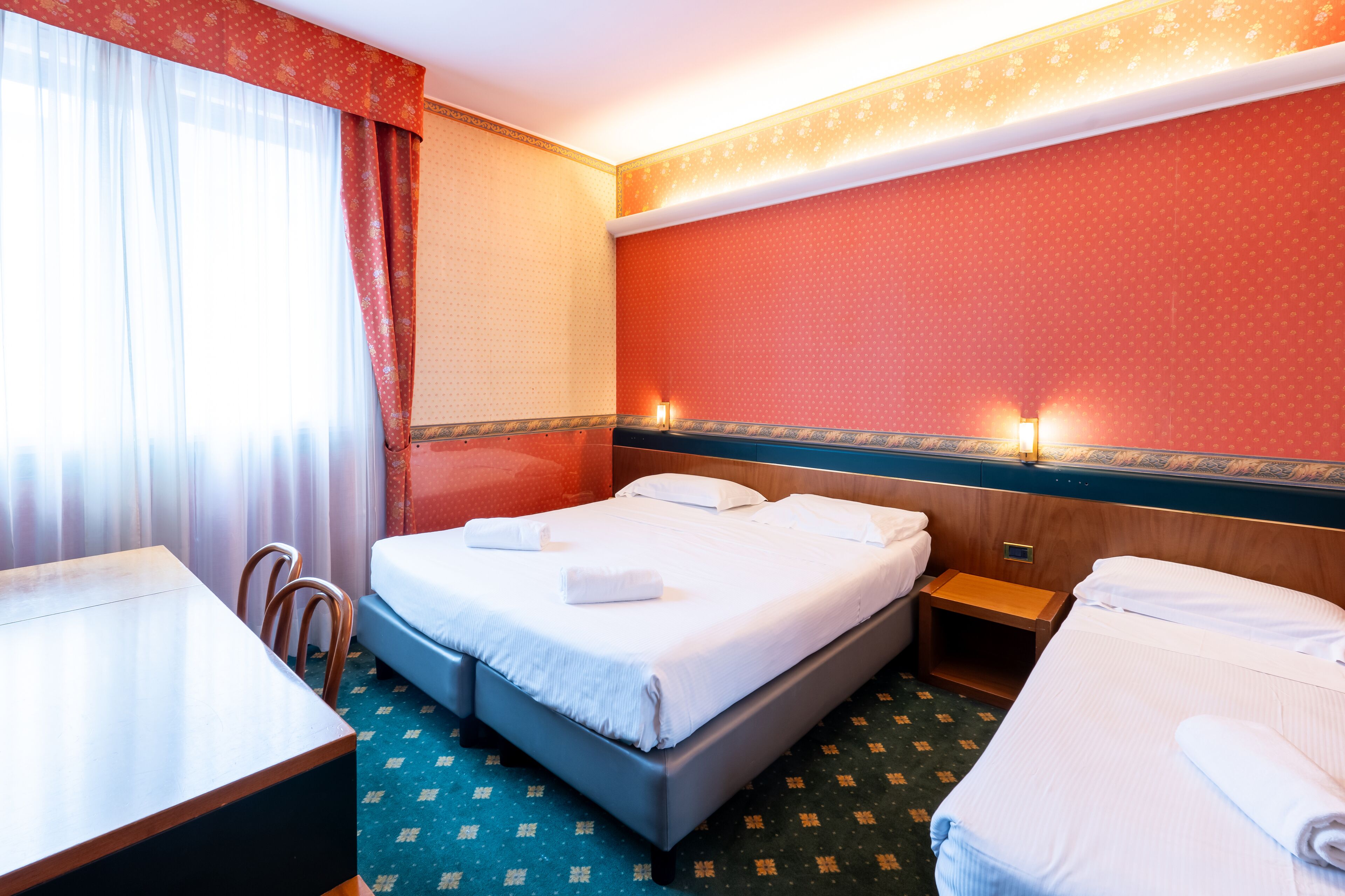 A hotel room with a bed, a desk, and a chair. There are two bedside tables and a nightstand.